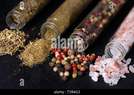 Massa assortiti spezie in bottiglie su ardesia scura sullo sfondo di pietra Foto Stock