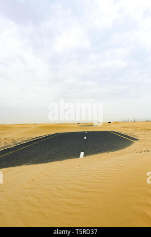 (Fuoco selettivo) vista mozzafiato di una strada deserta coperta da dune di sabbia. Empty Road che attraversa il deserto di Dubai durante il tramonto. Dubai. Foto Stock