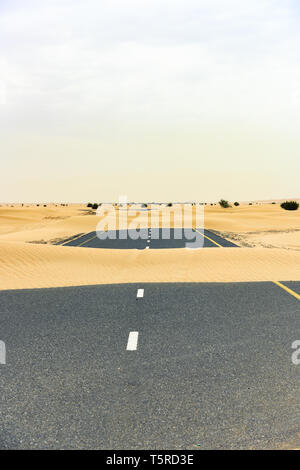 (Fuoco selettivo) vista mozzafiato di una strada deserta coperta da dune di sabbia. Empty Road che attraversa il deserto di Dubai durante il tramonto. Dubai. Foto Stock