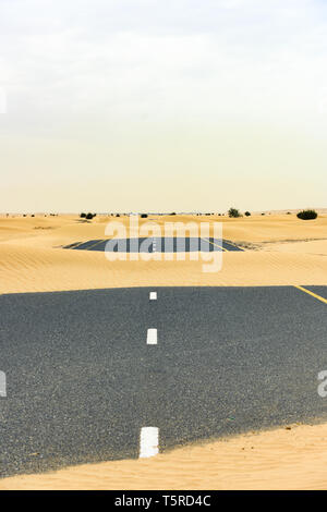 (Fuoco selettivo) vista mozzafiato di una strada deserta coperta da dune di sabbia. Empty Road che attraversa il deserto di Dubai durante il tramonto. Dubai. Foto Stock