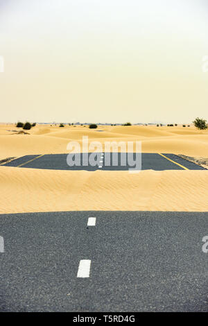 (Fuoco selettivo) vista mozzafiato di una strada deserta coperta da dune di sabbia. Empty Road che attraversa il deserto di Dubai durante il tramonto. Dubai. Foto Stock