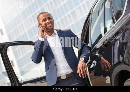 I giovani africani imprenditore americano in piedi accanto a AUTO parlando sullo smartphone sorridente allegro Foto Stock
