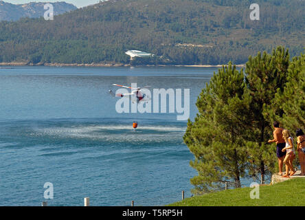 Fire Fighting elicottero con cestello bambi il caricamento di acqua sul mare e un gruppo di persone che guardano Foto Stock