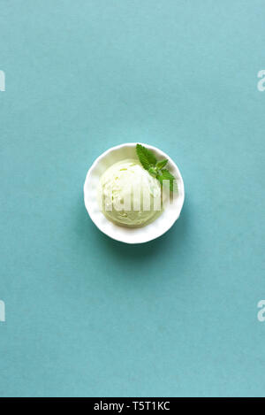 Verde Ice Cream su sfondo blu, vista dall'alto, copia dello spazio. Verde pistacchio, avocado o il tè verde gelato in tazza con foglia di menta. Foto Stock