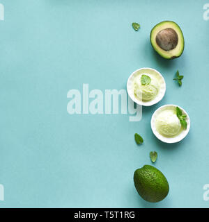 Avocado gelati su sfondo blu, vista dall'alto, copia dello spazio. Vegano verde avocado o gelato al pistacchio gelato con foglie di menta. Foto Stock