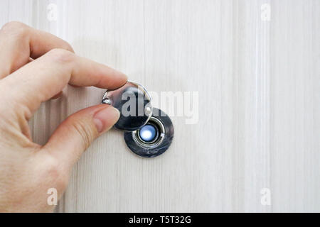 La mano si apre lo sportello del coperchio occhio magico nella porta anteriore di rovere chiaro. Foto Stock