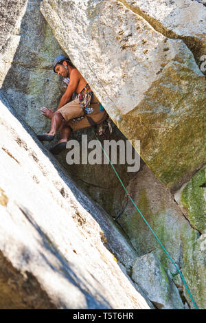 Un scalatore di opere il suo modo su un camino su una roccia salita denominata "uomo vecchio" in poco fumo scogliere vicino Squamish, BC, Canada. Foto Stock