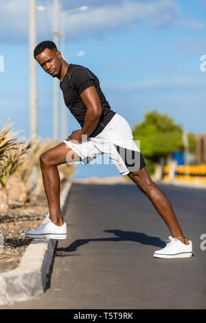 Il nero americano africano giovane stretching dopo il jogging all'aperto Foto Stock