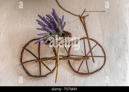 Millefiori viola sul piccolo ornamento di biciclette fatte a mano con sottili rami di albero appeso su un vecchio muro Foto Stock