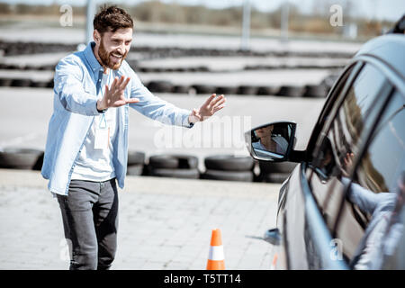 Istruttore di sesso maschile che mostra fermo con le mani mentre l'insegnamento per il parcheggio di un'auto sulla massa di formazione presso la scuola Foto Stock