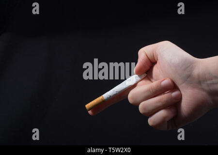 Mano che regge una sigaretta come pistola su sfondo nero Foto Stock