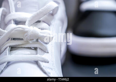 Vicino la stringa di moda bianco sneaker con nero scarpa in background. Foto Stock