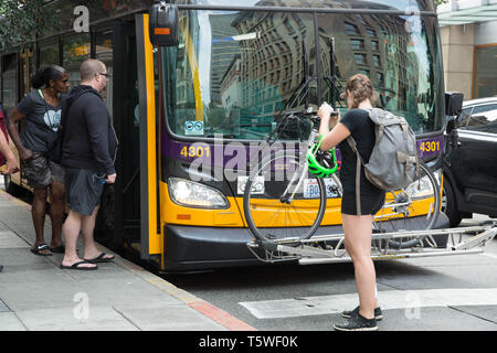 Persone di prendere un autobus di città in attesa in spire e una giovane donna caricando la sua bicicletta sulla parte anteriore del bus nel centro cittadino di Seattle, Stati Uniti d'America. Foto Stock