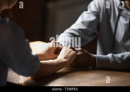 Chiudere fino a mani diverse giovane seduta a tavola tenendo le mani Foto Stock