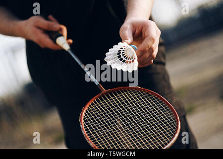 Un uomo vestiti di nero tenendo un racket e sta per lanciare un volano. Una piacevole attività outdoor è la riproduzione di badminton in una giornata di sole. Foto Stock