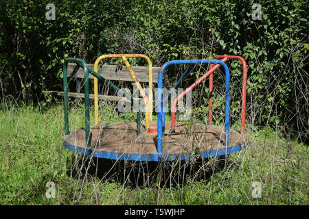 Vecchio arrugginito parco giochi merry-go-round e ricoperta di piante avvizzite nel parco abbandonati. Foto Stock