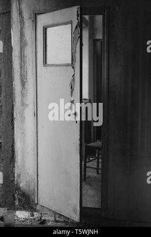 Aperto a metà scricchiolio porta che conduce dalla cucina al corridoio nella vecchia casa abbandonata interni. In bianco e nero. Foto Stock