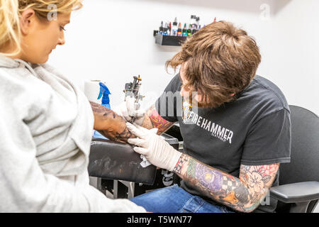 Una giovane donna siede mentre un tattooist lavora sull'aggiunta di un design per il suo "sleeve". Chepstow street e persone Foto Stock