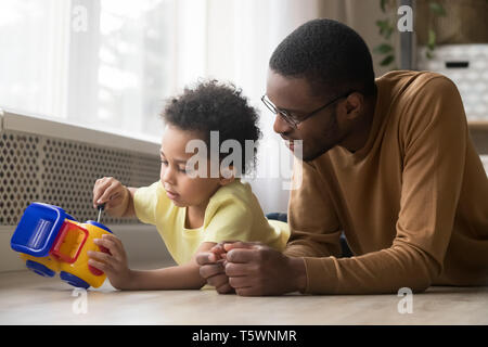 Carino figlio e padre africano insieme giocando riparazione carrello giocattolo Foto Stock