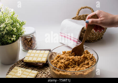 Una donna che fa 3 torta di cioccolato torta ingredienti sul tavolo. Cucina con bianco, cioccolato fondente e al latte. Le nocciole jar. Biscotti di pasta Foto Stock