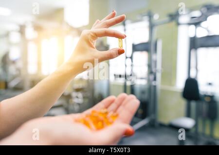 Primo piano della donna fitness mani mostra capsula di vitamina e omega-3,  palestra sfondo. Uno stile di vita sano, medicina, supplementi nutrizionali  e persone conc Foto stock - Alamy