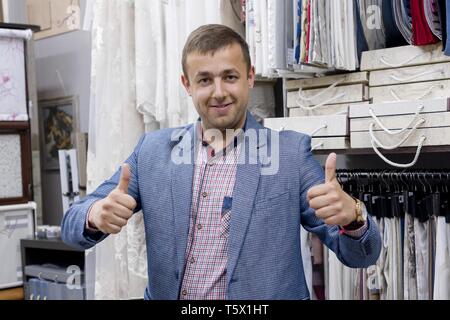 Fiducioso giovane imprenditore positivo tessuto il proprietario del negozio che mostra Thumbs up, gesto segno ok. Uomo in piedi nel negozio di sfondo tessuto interno sampl Foto Stock