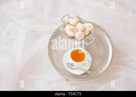 Vassoio di argento con una tazza di tè e macarons su una tavola di legno tavolo bianco in una camera bianca Foto Stock