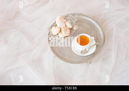 Vassoio di argento con una tazza di tè e macarons su una tavola di legno tavolo bianco in una camera bianca Foto Stock