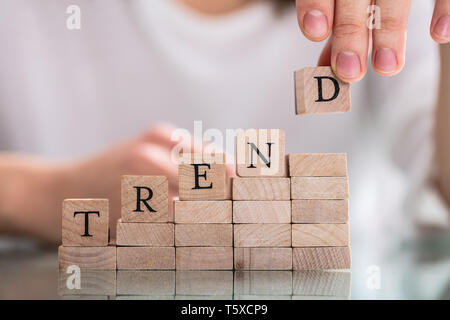 Persona della mano che trattiene i blocchi di legno ponendo ultimo alfabeto della parola tendenza riflessiva sulla scrivania Foto Stock