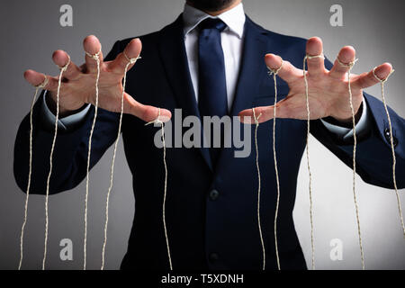 Mano d'uomo controlla il fantoccio con le dita attaccata al thread contro uno sfondo grigio Foto Stock