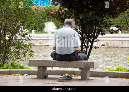 Il cinese vecchio uomo gente seduta da sola sul banco di pietra e relax nel giardino pubblico al Parco Zhongshan Park in Shantou city o Swatow City il 9 maggio 2018 Foto Stock