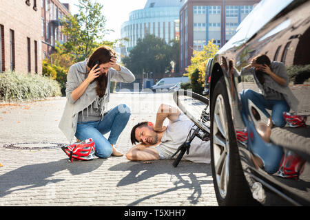 Giovane donna chiamando ambulanza dopo colpire ciclista maschio accidentalmente con la sua automobile Foto Stock