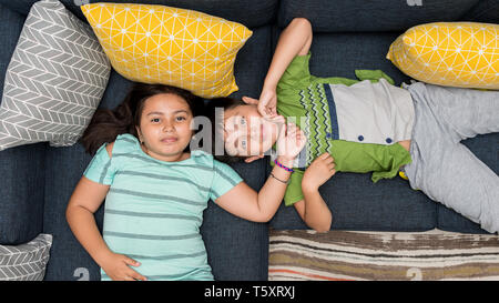 Miscelati asiatico/caucasian fratello e sorella e la posa sul divano insieme sorridente guardando direttamente alla fotocamera. Foto Stock