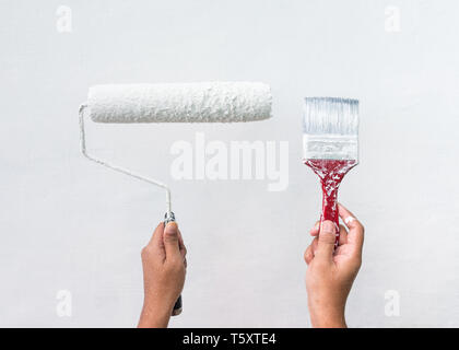 Donna che mantiene fino vernice usata e la spazzola a rullo con vernice bianca e muro bianco sullo sfondo. Foto Stock