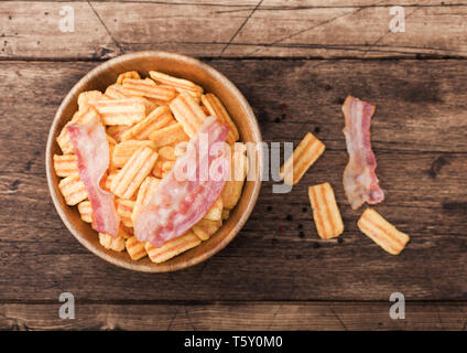 Bacon aromatizzati spuntini chip nella ciotola di legno con grigliate di fette di bacon su uno sfondo di legno. Foto Stock