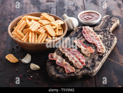 Bacon spuntini aromatizzato con grigliate di fette di bacon su vintage tagliere con aglio e salsa su uno sfondo di legno. Foto Stock