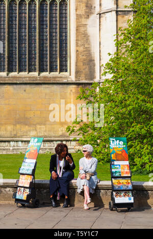 Due testimoni Jehovahs Signore seduto sul muro di Kings College Chapel, con il cinese e inglese opuscoli. Città universitaria di Cambridge Foto Stock