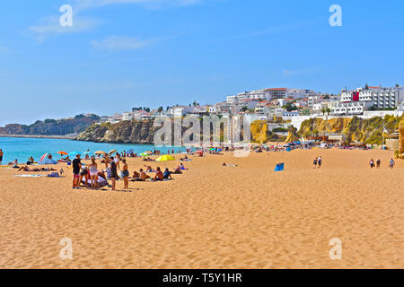 Folle estive godendo il sole sulla spiaggia principale di sabbia dorata, adiacente alla città vecchia di Albufeira nella regione dell'Algarve Portogallo Foto Stock