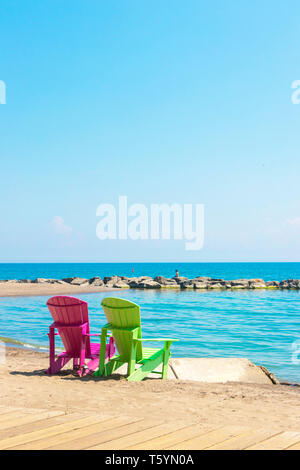 Due luminose terrazze colorate o sedie da spiaggia di Kew balmy spiaggia che si affaccia sul lago Ontario a Toronto Est, Canada Foto Stock