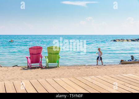 Il ragazzo adolescente cammina accanto a due luminose terrazze colorate o sedie a sdraio presso la spiaggia KeywBalmy che si affaccia sul lago Ontario a Toronto est, Canada Foto Stock