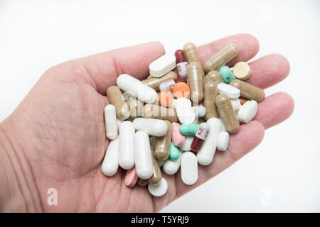 Una mano che tiene una grande quantità di farmaci - farmaco in pillole, capsule ed in forma di pastiglia contro uno sfondo bianco Foto Stock