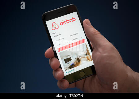 Un uomo guarda al suo iPhone che visualizza il logo Airbnb (solo uso editoriale). Foto Stock