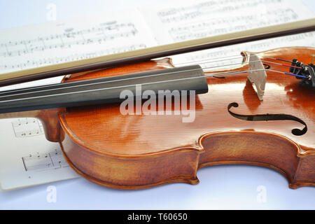 Vista da vicino a un nuovo legno bruno violino con un inchino messo lungo la strumento musicale e di un foglio di musica al di sotto di esso. Foto Stock