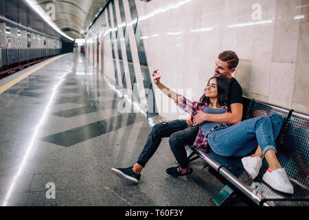 Giovane uomo e donna utilizzare la metropolitana. Matura in metropolitana. Giovane donna prendendo selfie di se stessa e il ragazzo a svuotare la stazione della metropolitana. Il sorriso e posa. Amore Foto Stock