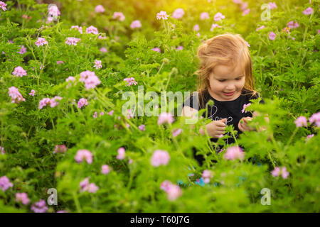 Ragazza sorridente in piedi in mezzo a piante in fiore in una giornata di sole in campagna Foto Stock