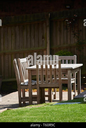 La luce del sole splende tra iroko in legno tavolo e sedie su un patio nel giardino. Foto Stock