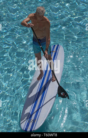 Senior Standup-Surfer in hellblauem klaren Wasser von oben - il SUP sport come sport per il tempo libero di tutte le età: senior in piedi sul SUP PENSIONE da sopra Foto Stock