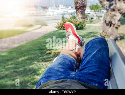 Un uomo in abiti estivi e sneakers è sdraiato su una panchina nella stagione calda. Foto Stock