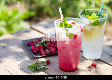 Bevanda fredda. Dissetante bevanda estiva limone, dissetante bevanda estiva lampone con basilico e il ghiaccio su una cucina in legno tavolo. Foto Stock