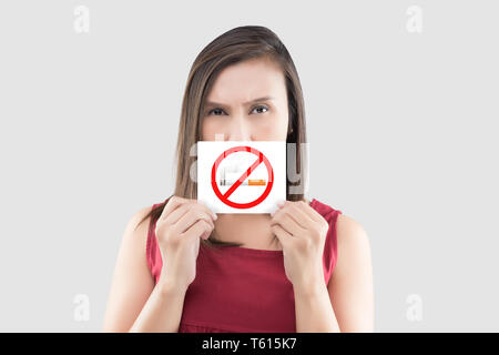 Donna asiatica in rosso camicetta holding è vietato fumare sul libro bianco contro uno sfondo grigio. Immagine della donna con una fumatori segno di restrizione. Foto Stock